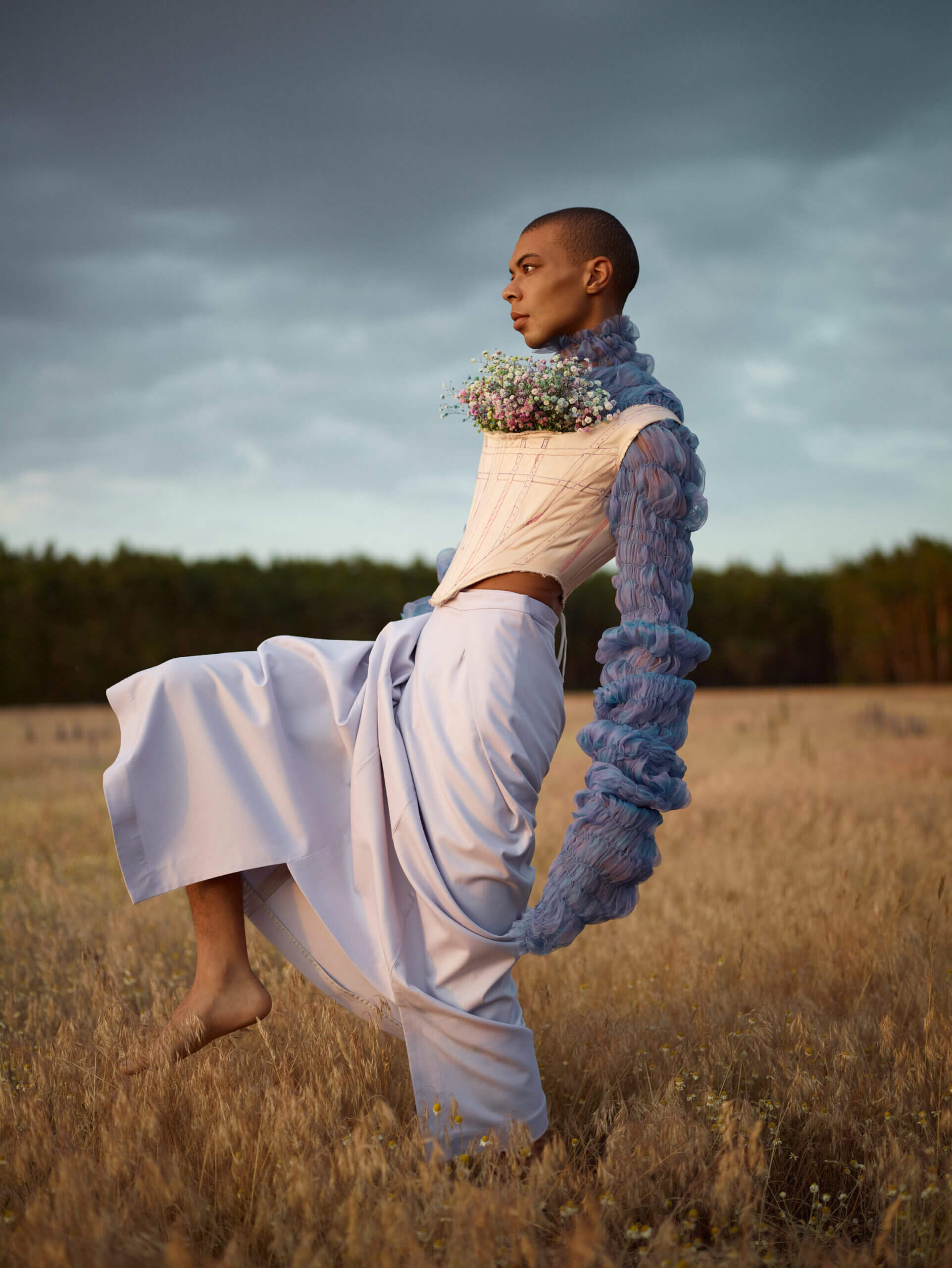 Ein Mann in einem weißen Kleid und Blumenkorsett tanzt auf einem Feld