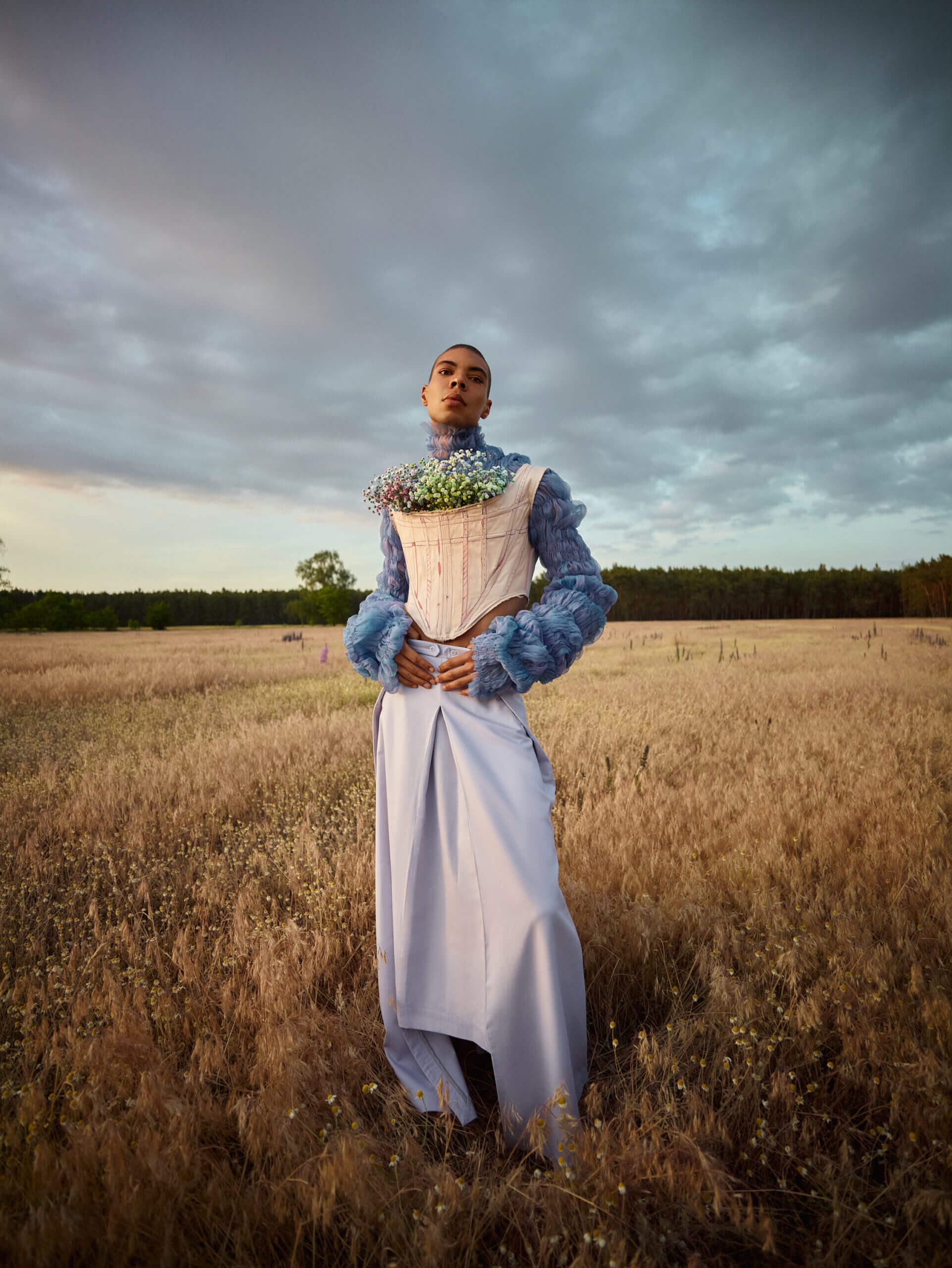 ein Mann mit Blumencorset in einem Kleid, der auf einem Feld steht